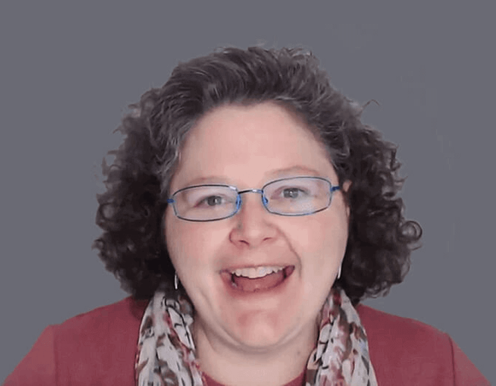 Shannon Medisky smiling wearing glasses, a pink shirt, and a scarf covered in flowers